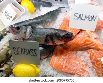Rough Handwritten Labels Alonsgide Sea Bass And Salmon Fish On Ice On A Market Stall. No People. 