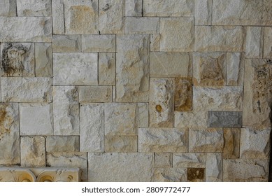 Rough natural stone wall texture background with irregular rectangular blocks in cream, beige and ochre tones, featuring rustic cut stone masonry pattern with visible mortar joints