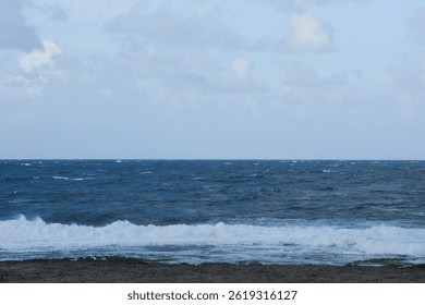 Rough Ocean Waves Impacting a Rocky Beach: A powerful scene of wind-driven ocean waves crashing and creating sea spray as they hit a dark, rocky shore.