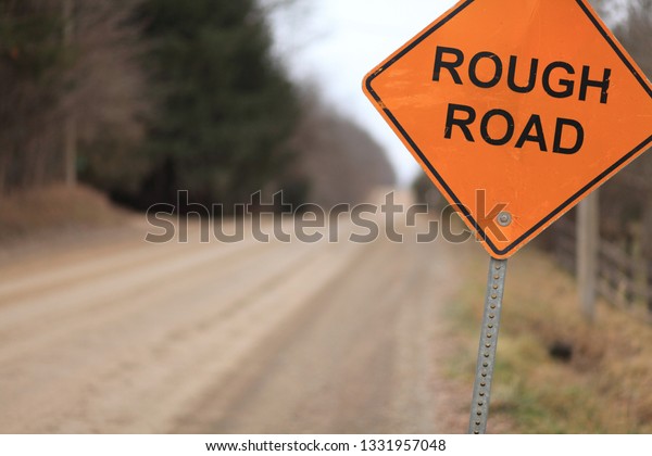 Rough Road\
sign on the side of a rough unpaved\
road.
