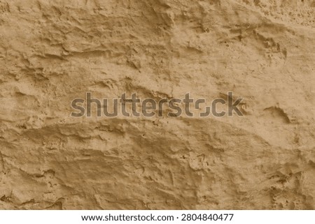 a rough sandstone cliff wall featuring a rich earthy texture. The surface is characterized by irregular crevices, grainy details, and eroded patterns in warm ochre, beige, and tan tones