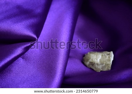 Rough spodumene aka triphane unsharp on satin magenta purple background.Draped magenta purple fabric with spodumene in the background.