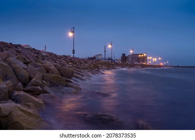 Rough Stone Coast Of Salthill, Galway City Ireland. Blue Hour. Town Illumination Reflects In Calm Water Of The Ocean. Calm And Peaceful Scene.