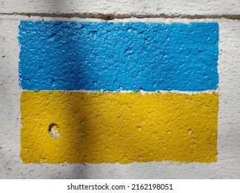 Rough wall with national flag of Ukraine country. Blue yellow flag painted on wall surface. Closeup Ukrainian flag paint on stone texture with shadows in sunlight. Symbol of independence and freedom