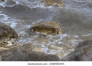 Rough waves crashing on the boulders on the rocky shore during a gray overcast autumn day.
