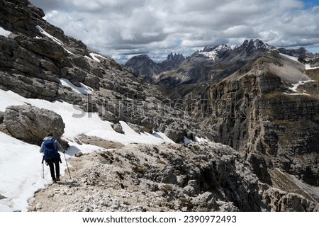 Rough and wild landscape in the Italian Dolomites: Young sporty female hiker next to a snowfield in iconic Puez Odles Nature Park near Gardena Valley in South Tyrol, Alto Adige.