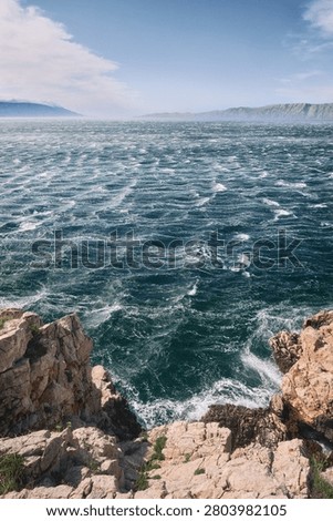 Rough wind driven sea with whitecaps below rocky cliffs and distant mountains in Croatia.