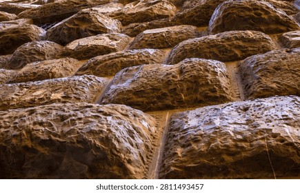 Rough-hewn stone blocks of a rusticated masonry wall in raking light. Craftsmanship and durability of historical stonework.