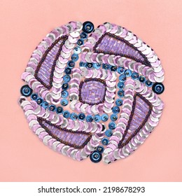 Round abstract geometric pattern embroidered with sequins and glass beads in silver, blue and violet colors over pink sateen fabric - Powered by Shutterstock