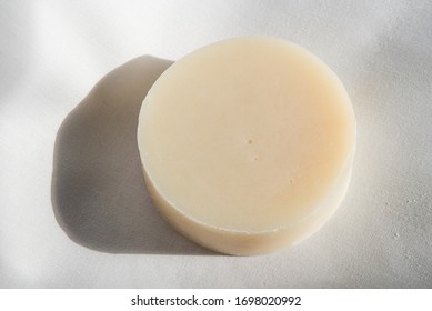 A Round Bar Of Light-colored Natural Soap On A Plain White Background.