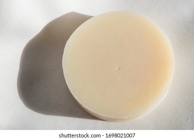 A Round Bar Of Light-colored Natural Soap On A Plain White Background.