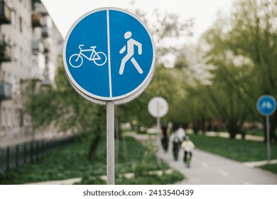 a round blue road sign with a pedestrian and a bicycle, blurred pedestrians and cyclists in the background. paved path in the park
