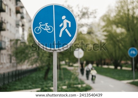 a round blue road sign with a pedestrian and a bicycle, blurred pedestrians and cyclists in the background. paved path in the park