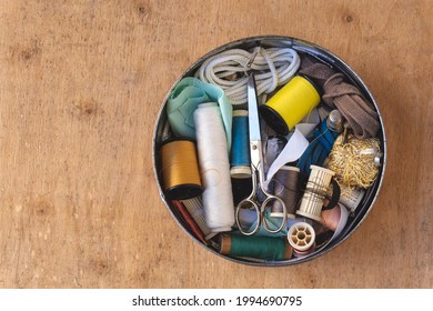 Round brass box, with sewing utensils, on a wooden background. 