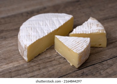 Round Brie cheese with a section cut out over wooden background, close up view.