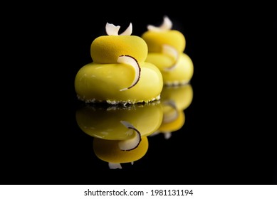 Round Cake In Yellow Glaze Decorated With Pieces Of Coconut On A Black Background.