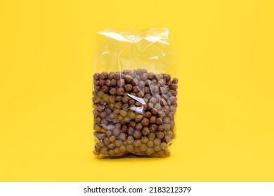 Round chocolate flakes in a transparent package on a yellow background. The packaged cereal food product is in the center of the image. Transparent packaging with round flakes in the form of balls - Shutterstock ID 2183212379
