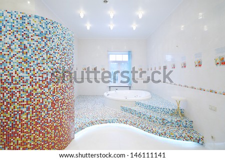 Round clean jacuzzi and stairs in spacious white bathroom with tiles with poppies.