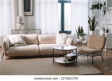 Round Coffee Table In Front Of Beige Sofa With Pillows And Armchair In Living Room Interior With Console Table And Flowers In Vase