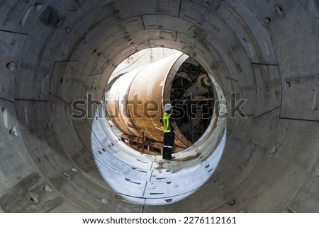 Round concrete elements or segment of a built subway tunnel under construction. Tunnel boring machine on construction site building metro with engineer to control.