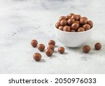 Round crunchy milk chocolate candies in white bowl on light background. Best sweet snack