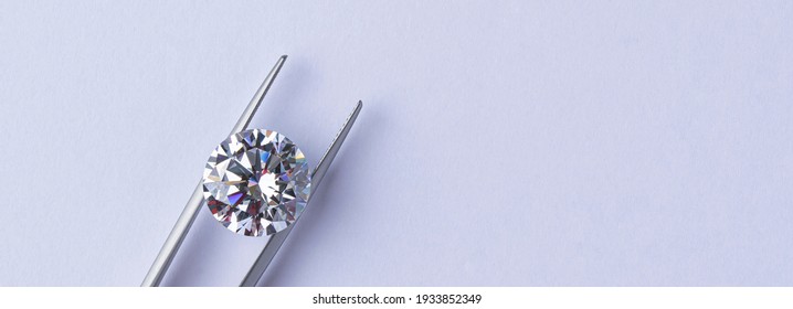 Round cut diamond in tweezers. Top view of diamond with copy space on light background.