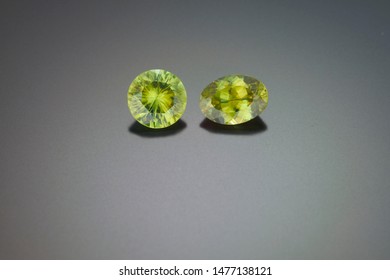 A round cut and an oval cut peridot gemstones are shown on a grey reflective background.