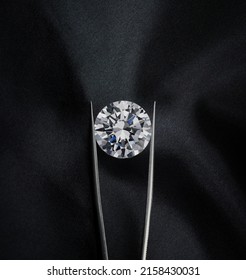 Round Diamond Held in Tweezers Upright on Luxury Black Background.   