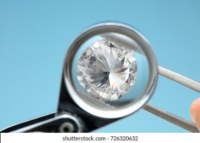 Round diamonds is being looked through a 10x loupe top on blue background. It shows many flaws easily visible through the loupe back side