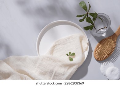 A round dish decorated with a white towel, cotton pads, wooden brush and a glass vase with tree branch. Empty space for natural beauty product advertising