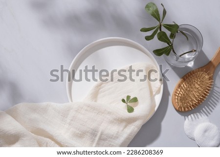 A round dish decorated with a white towel, cotton pads, wooden brush and a glass vase with tree branch. Empty space for natural beauty product advertising