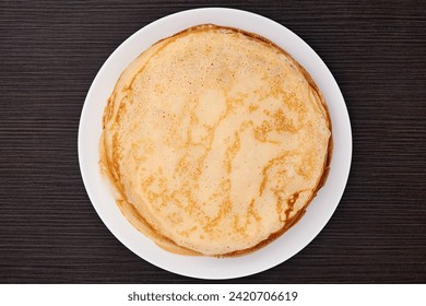 A round dish with fried pancakes on a brown table. Sweet dessert. Top view. - Powered by Shutterstock