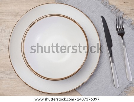 Round empty white ceramic plate, knife and fork on the table, top view