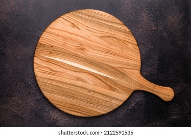 Round Empty Wooden Charcuterie Serving Board With Handle On Old Dark Brown Shabby Table. View From Above. Top View. Food Background. Template With Copy Space For Text. Flat Lay, Mockup. Layout, Frame.