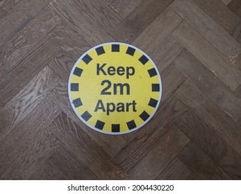 A Round Floor Sign With Black Text On Yellow Background.It Says Keep 2 M Apart .Coronavirus Pandemic