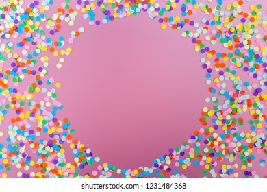 Round frame of colorful confetti on pink background. 