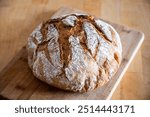 Round, freshly baked homemade bread with a golden, crispy crust. The bread has characteristic cuts on the surface, which add to its rustic charm.