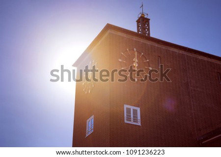 Round golden alarm clock on red brick house against sunlight. The image of the vintage clock shows noon midday 12 twelve - concept timer standard time change alert retro clock design hour signal