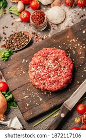 Round ground beef portioned beef patty made from beef mince on a wooden board. Hamburger meat seasoned and ready for a barbecue.Spices and condiments for a grill.Homemade burger recipe.Prepared burger