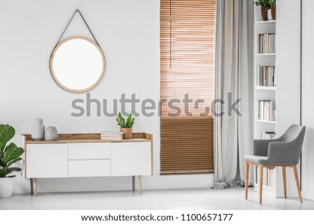Round hanging mirror on the white wall above a cabinet in a bright contemporary room interior. Real photo.