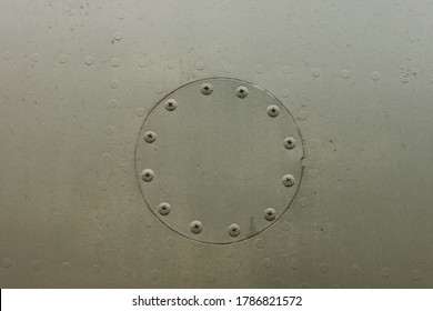 Round Hatch With Rivets Of An Old Camouflage Surface With Green Color On A Military Aircraft. Fragment Of A Fuselage Of An Old Jet Fighter