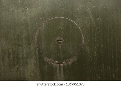 Round Hatch With Rivets Of An Old Camouflage Surface With Green Color On A Military Aircraft. Fragment Of A Fuselage Of An Old Jet Fighter