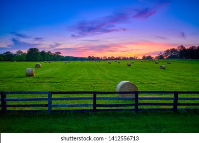 Round hay bails in a field at sunset with fence in the foreground.