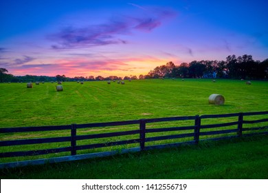 Round hay bails in a field at sunset with fence in the foreground.