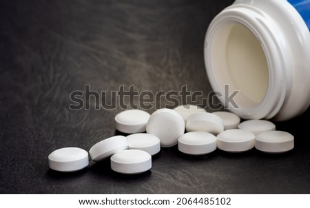 round herbal white tablets poured from a white bottle on a dark,black background. natural herbs, organic pills, vitamins from medicinal plants, calcium,antidepressants and painkillers
medicine concept