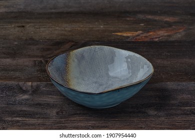 a round, high, empty plate of pastel color on a dark brown wooden background. Side view.
