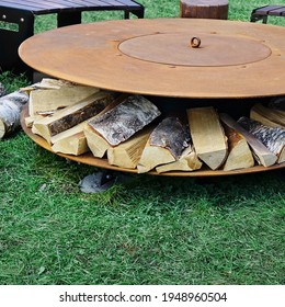 Round Iron Fire Pit Table On Patio In Backyard Garden. Steel Rounded Fire Pit With Grill Top On Backyard Party Place. Grill Appliance And Fireplace On The Back Yard Lawn.