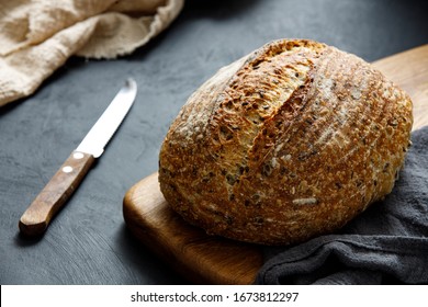 Round loaf of freshly baked sourdough bread with knife on cutting board. Artisan bread with seeds on dark table. Rustic sourdough bread. - Powered by Shutterstock