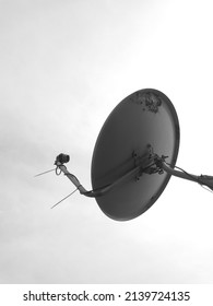 A Round Metal Antenna, A Pay Television Receiver, Facing Up Against The Sky In Black And White Photo.