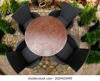 A round metal table, two black armchairs on the cobblestones. View from above.